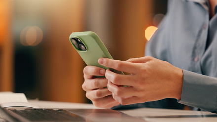 Person in shirt holding a phone in front of laptop