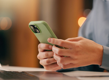 Person in shirt holding a phone in front of laptop