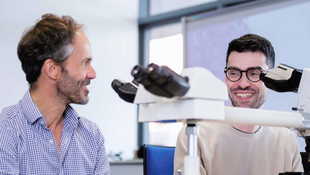 Two people at a microscope smiling