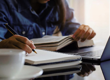 Student handwriting information on diary notebook while reading book