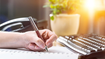 Person writing a report with a pen at their desk