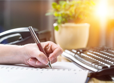 Person writing a report with a pen at their desk