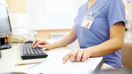 Person in scrubs at desk working on computer
