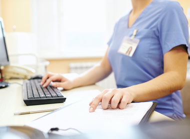 Person in scrubs at desk working on computer