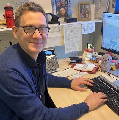Dr David Turner sat at his desk and smiling at the camera