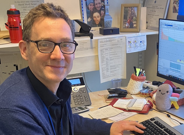 Dr David Turner sat at his desk and smiling at the camera