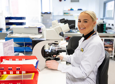 Smiling scientist at a microscope at a desk in a lab