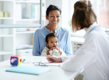 Person with baby sat on their lap talking to a doctor