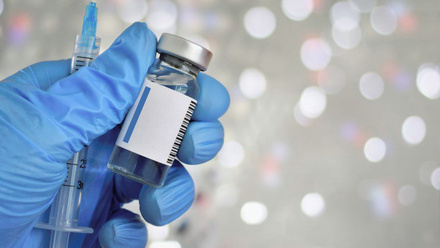 Blue gloved hand holding a vaccine vial and a syringe. 