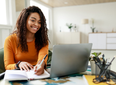 Student making notes and smiling sitting at a laptop