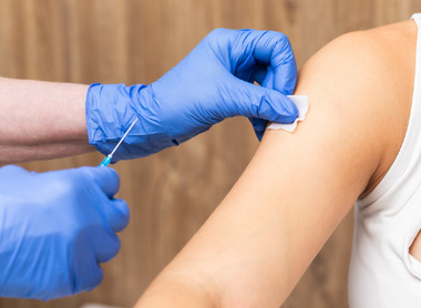 Medical assistant sanitizing a patient's arm with a cotton pad before injection of a vaccine
